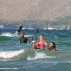 Thumb Picture: Eine Gruppe von Menschen, die auf einer Welle im Wasser hinter einem Drachen reitet.
