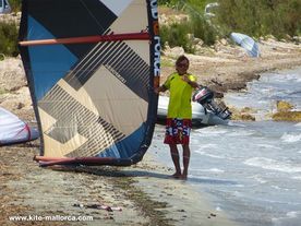 A man standing on a beach holding a kite and helping to launch it.
