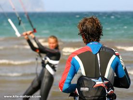 A girl on a beach holding a kite in front their instructor .
