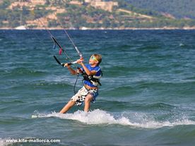 A child looking to his kite while riding on his kiteboard